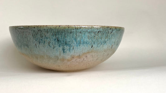 A generously sized stoneware bowl with gentle ripple texturing around the underside of the curve, glazed in a warm sandy tan that shifts to a rich blue-green verdigris near the rim and spills over into the interior of the bowl.